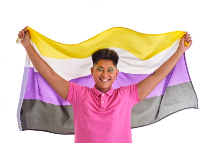 Non-Binary Asian person in a pink shirt holding the non-binary flag.