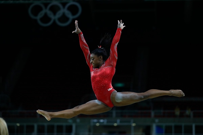 Simone Biles leaping in a red leotard.