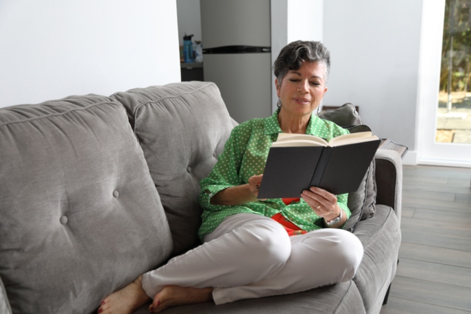 Latina woman reading a book on a gray couch