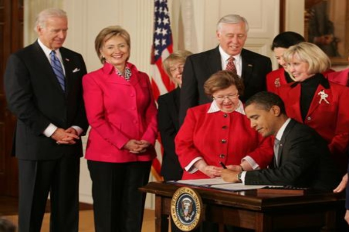 President Obama signing the act into law, Lilly standing behind him, surrounded by politicians and activists.