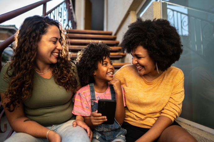 Interracial sapphic couple smiling with young Black girl.