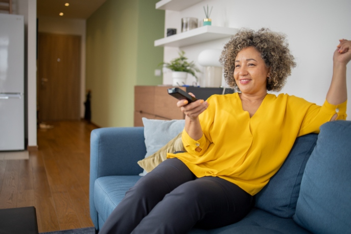 Black woman in a yellow shirt watching tv.