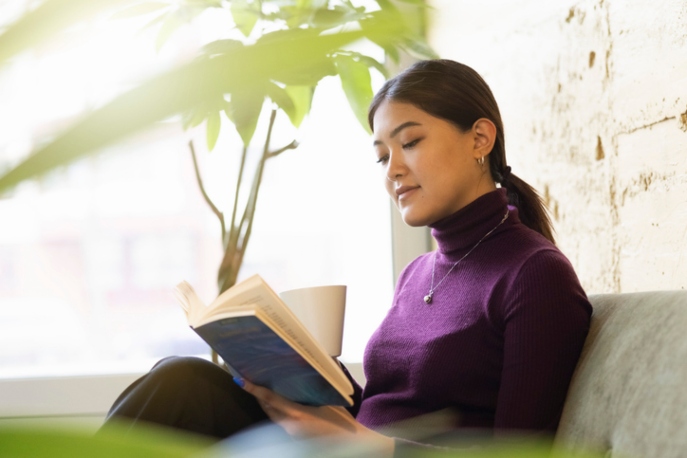 Asian woman in a purple turtleneck sweater reading a book